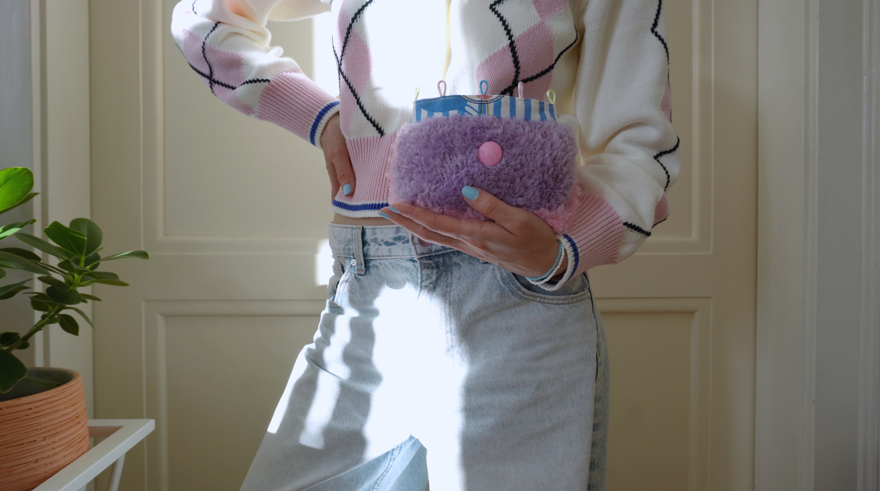 Person wearing a patterned sweater holding a fluffy purple purse with a pink button, standing indoors.
