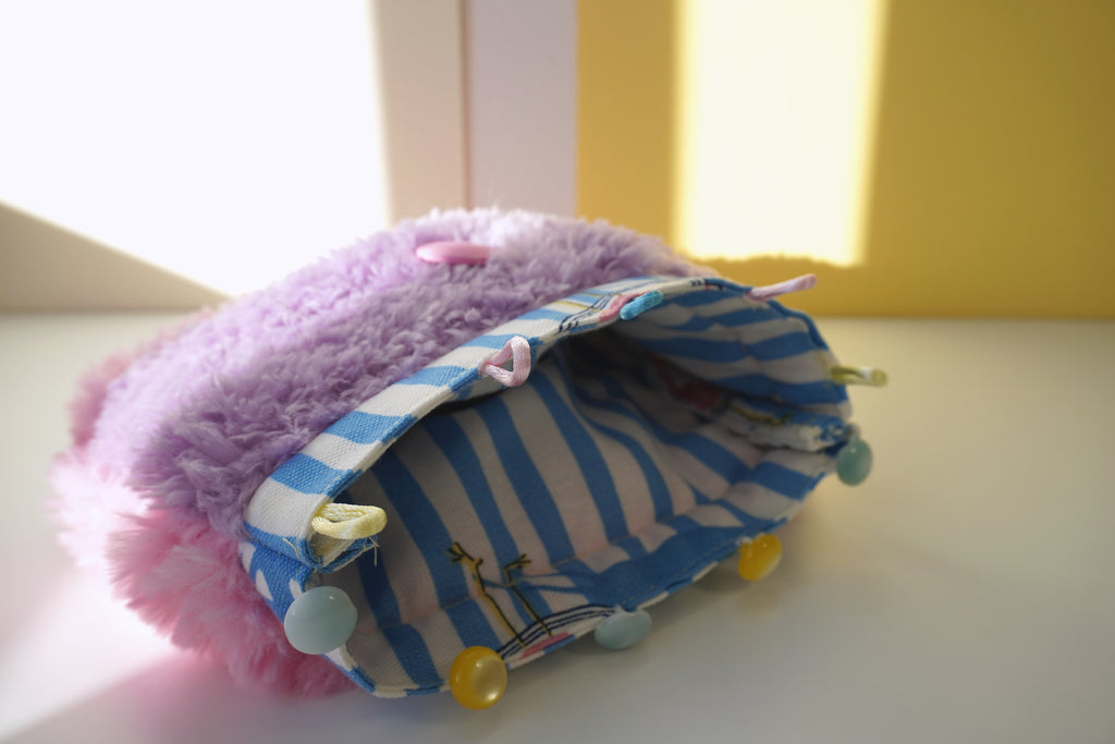 Small fluffy bag with striped patterned lining and yellow and blue buttons on a light surface