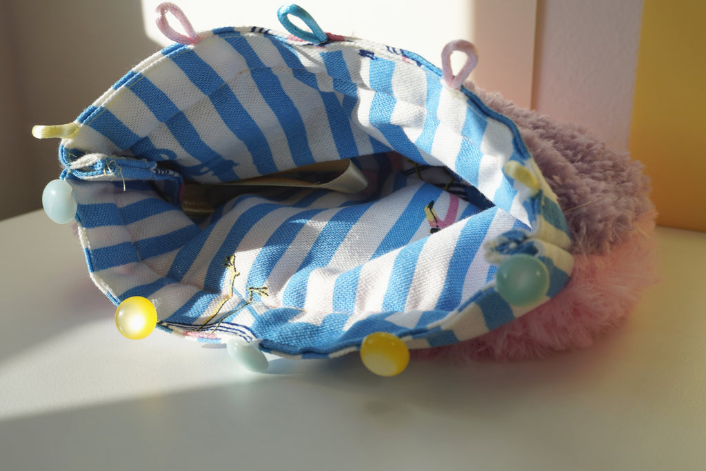 Blue and white striped lining of a fluffy purse with colorful buttons on a light surface