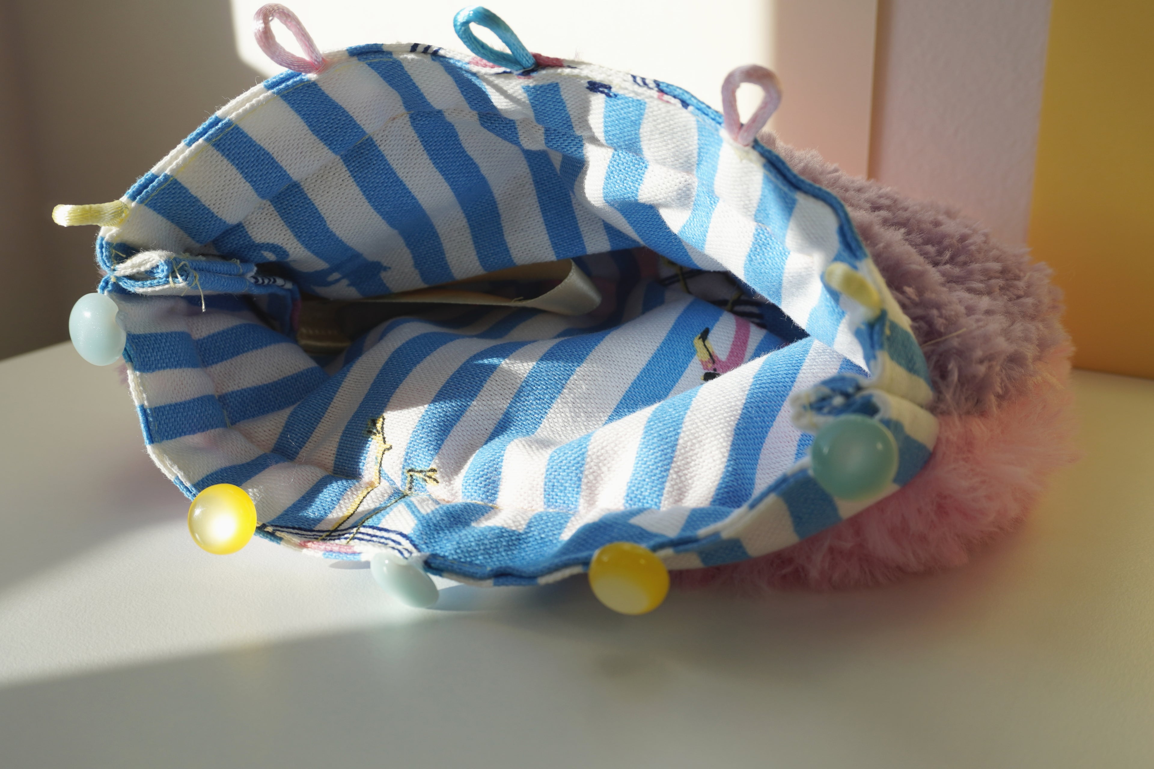 Blue and white striped lining of a fluffy purse with colorful buttons on a light surface