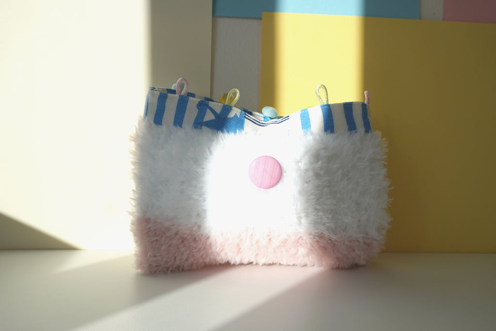 White and pink fluffy hand bag with blue and white lining and a pink button on a yellow wall background - SPOONITTO brand