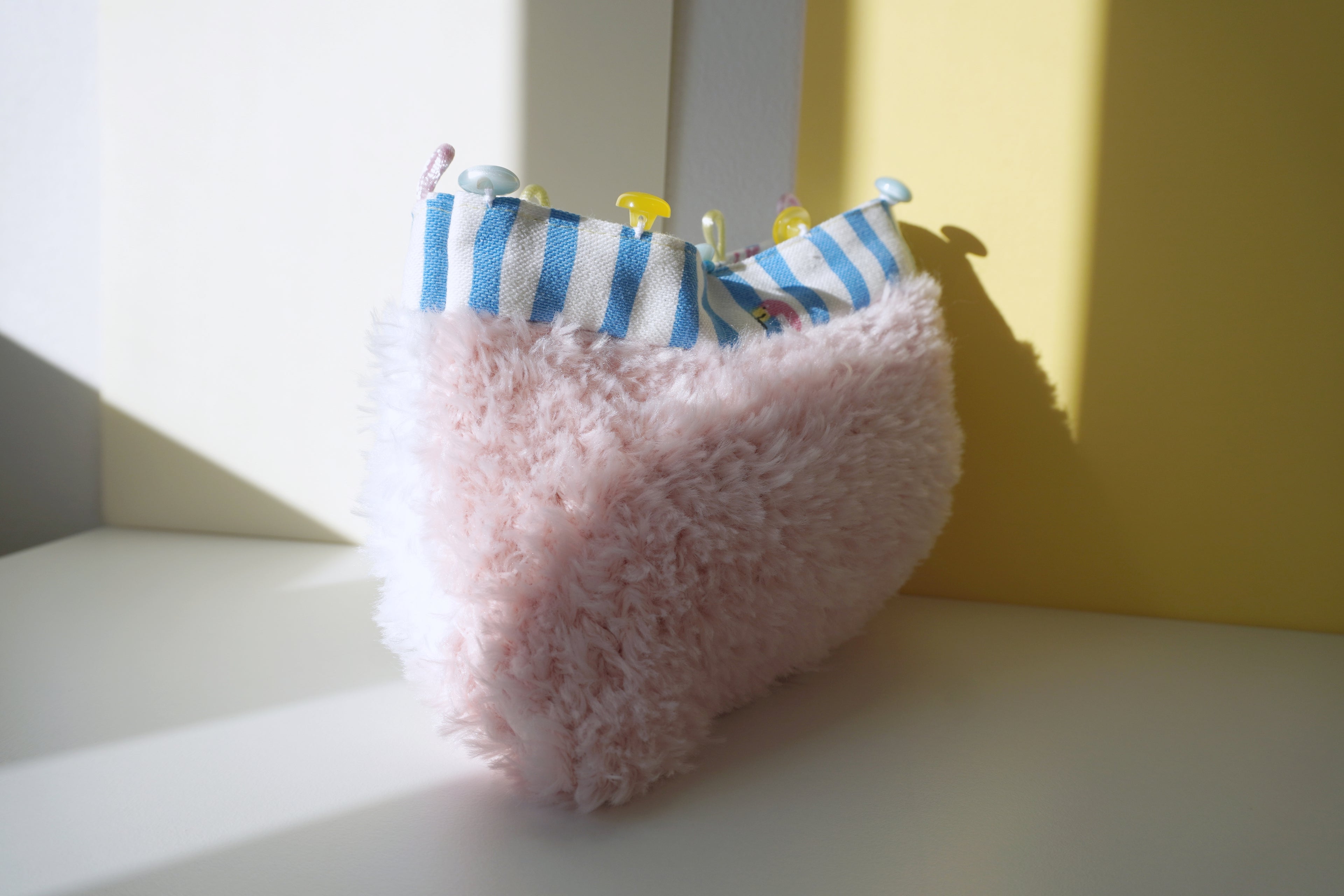 Pink fluffy small bag with blue and white striped lining  on a light surface.