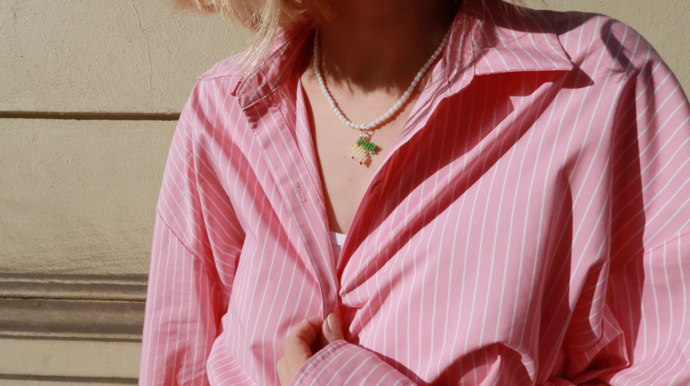 Person wearing a pink striped shirt and cute lemon necklace design with a neutral background