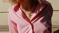 Person wearing a pink striped shirt with a necklace featuring a lemon pendant.