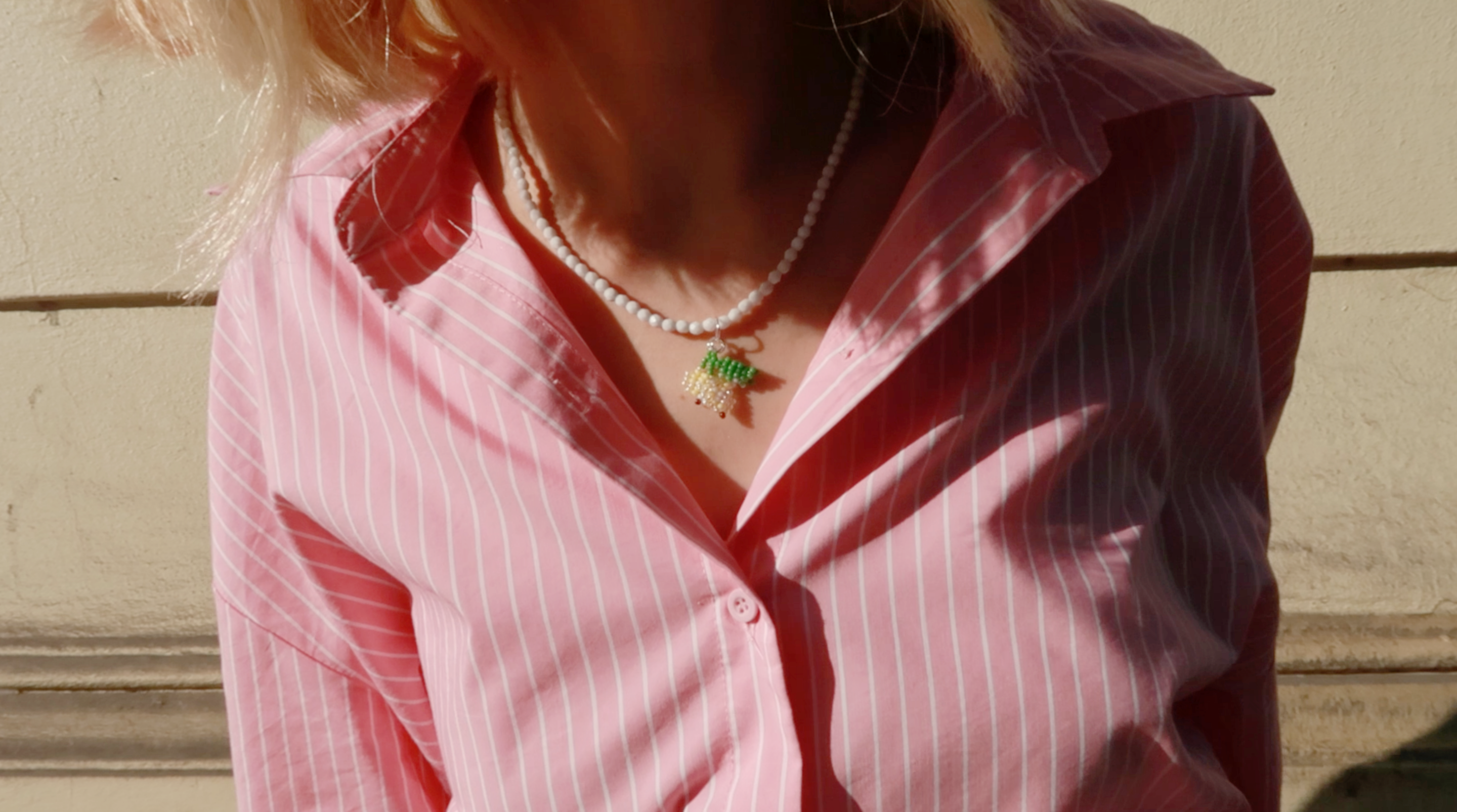 Person wearing a pink striped shirt with a necklace featuring a lemon pendant.