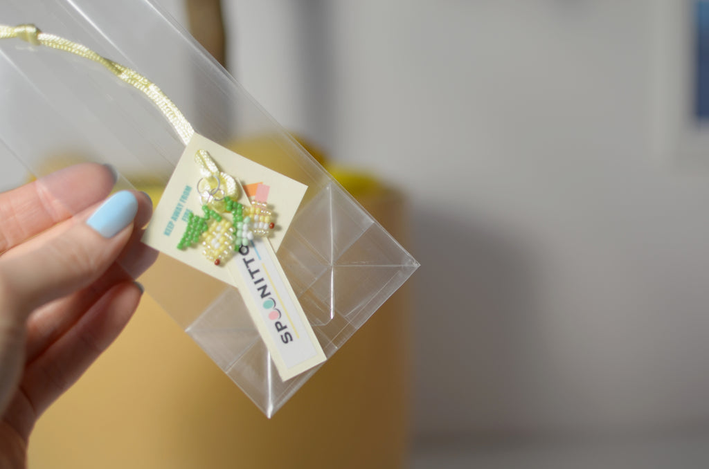 Hand holding a clear bag with a small lemons pendant and a branded card.