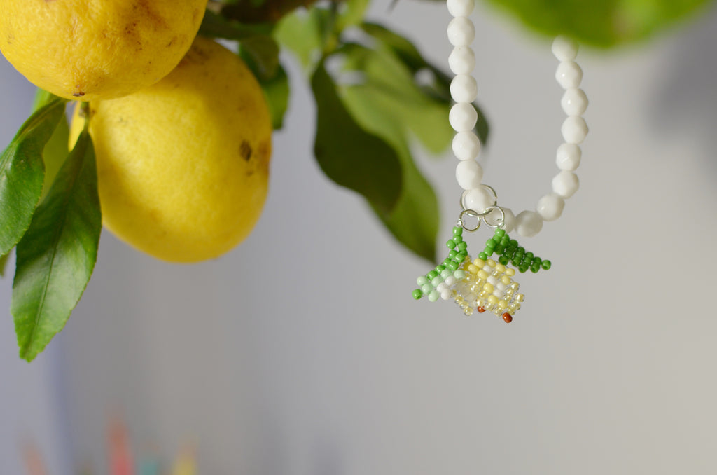 White beaded necklace with lemons pendant next to lemon tree