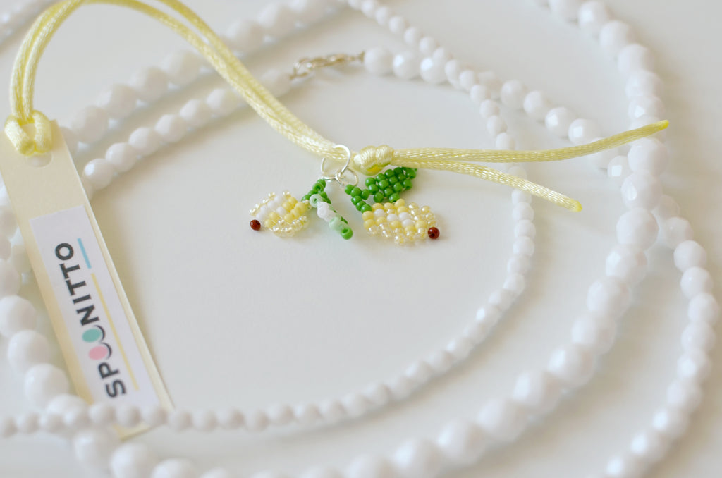 Necklace with beaded lemons pendant on a white textured surface, featuring the brand 'SPOONITTO'.