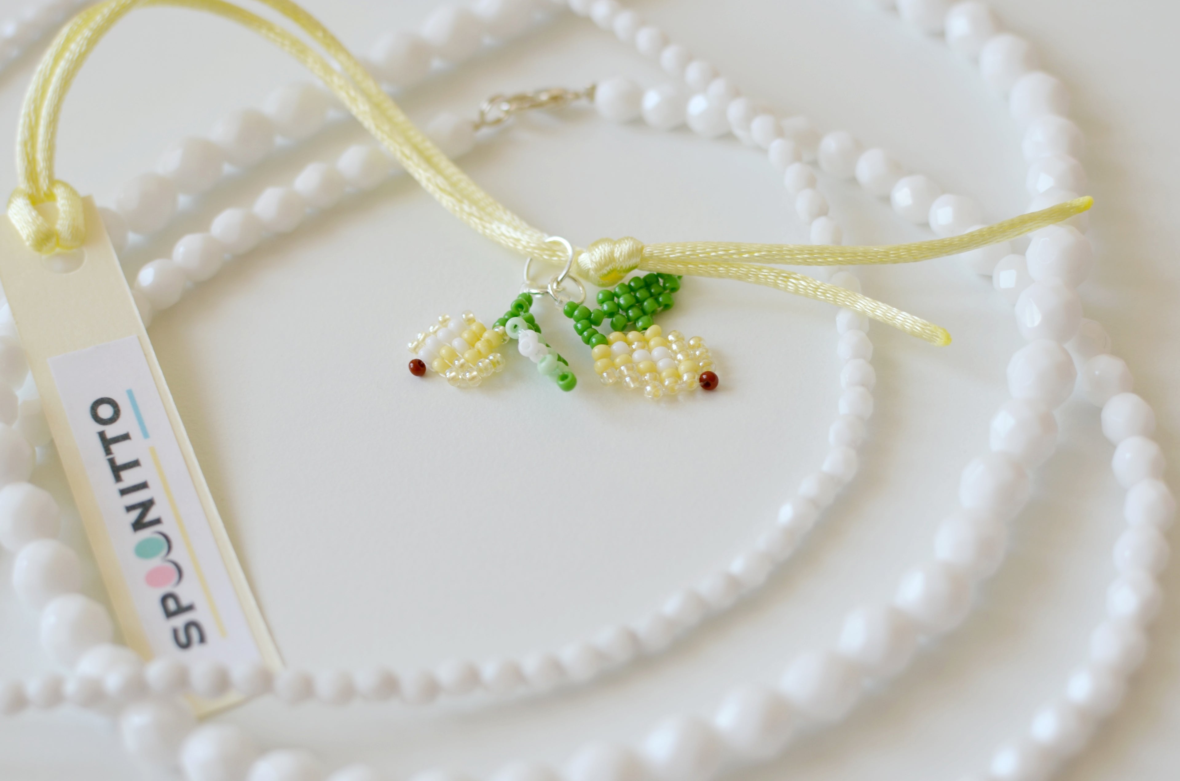 Necklace with beaded lemons pendant on a white textured surface, featuring the brand 'SPOONITTO'.