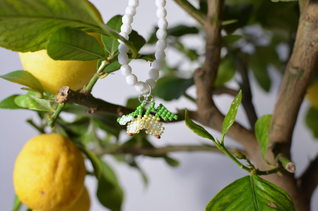 White necklace with beaded small lemons design hanging on a lemon tree branch.