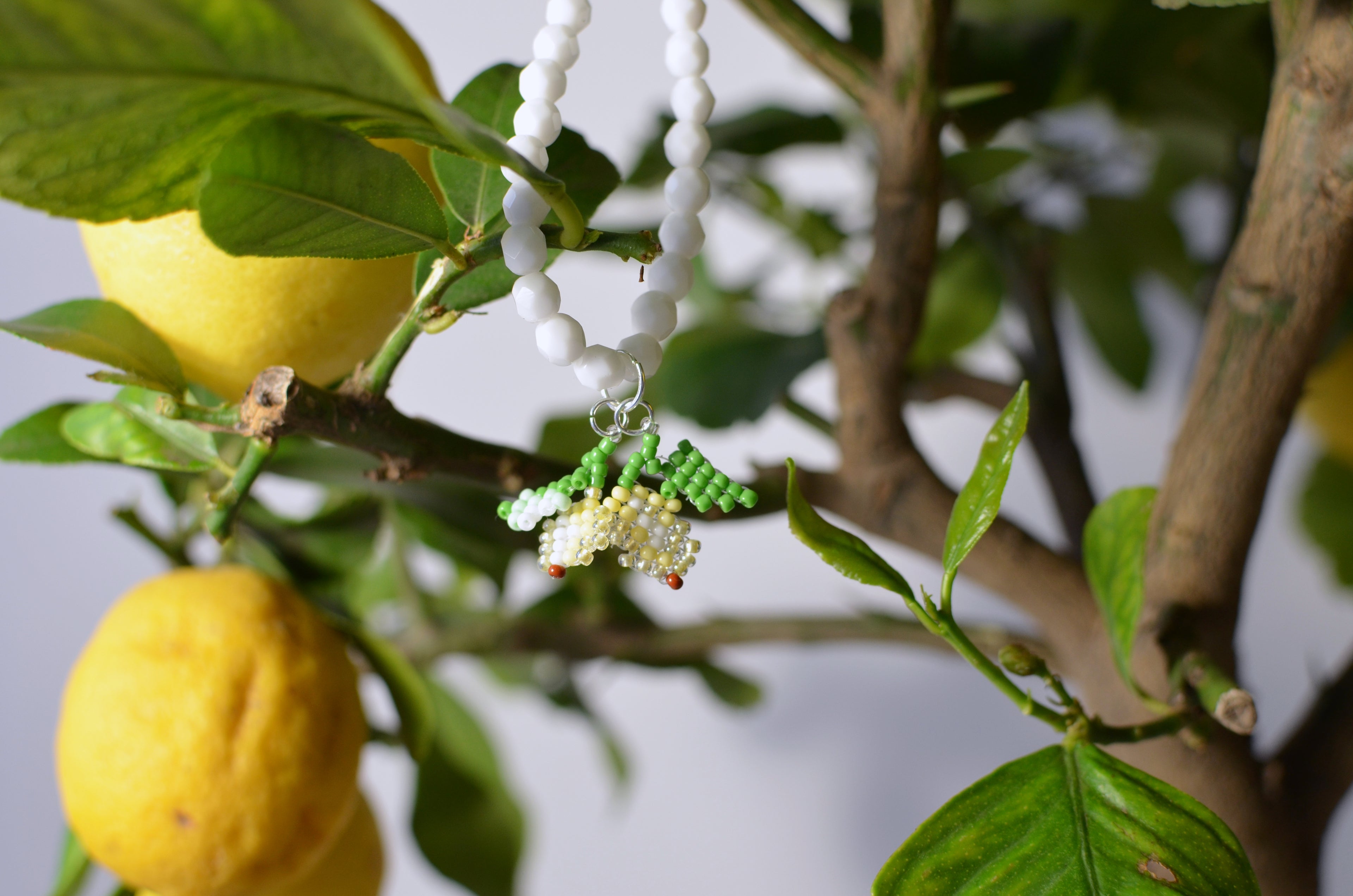 White necklace with beaded small lemons design hanging on a lemon tree branch.
