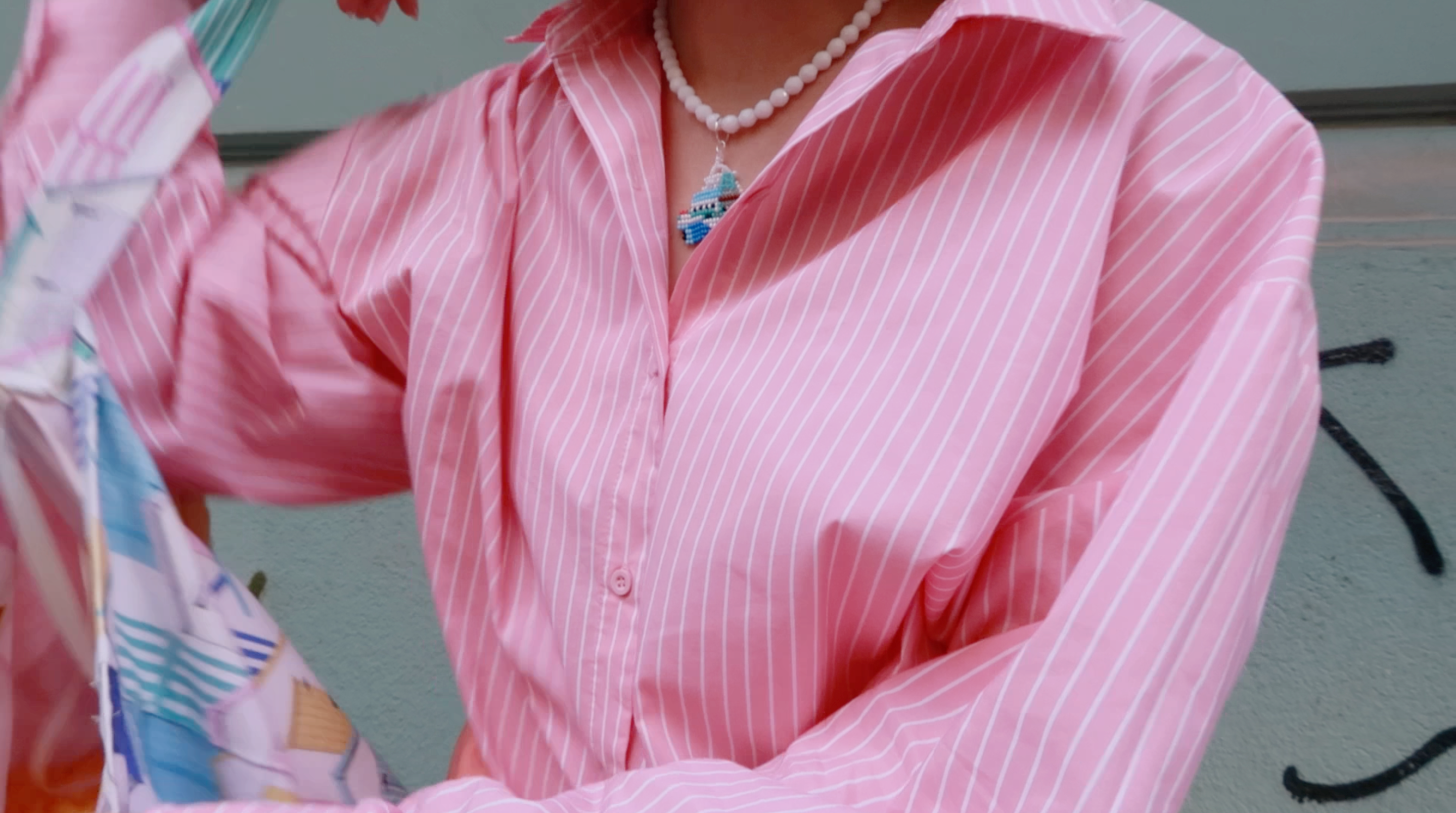 Person wearing a pink striped shirt with a necklace, holding a colorful bag.