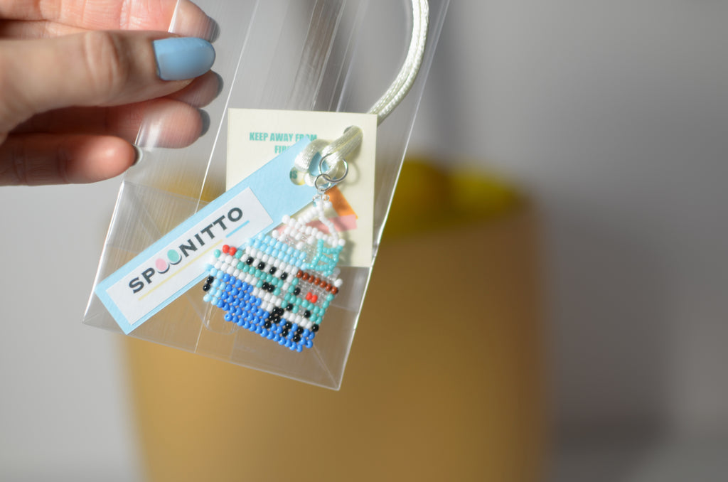 Hand holding a clear plastic bag with a pixelated ship pendant and a visible brand tag.