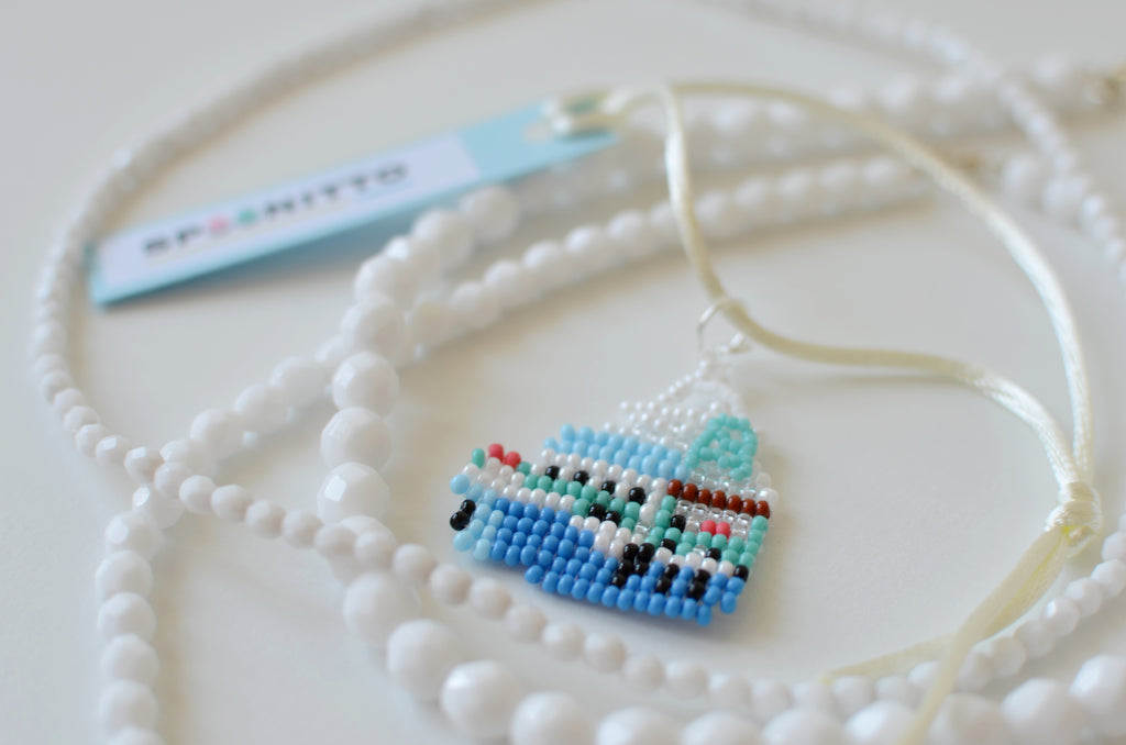 Beaded necklace with a small blue boat pendant on a white background